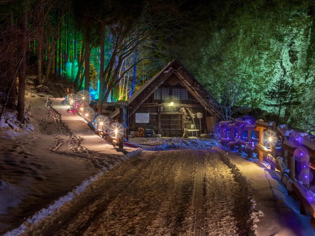 灯りに照らされた雪道と古民家
